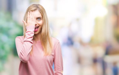 El yüz ve sürpriz duygu kendinden emin gülümseme ile tek gözüyle kapsayan izole arka plan üzerinde pembe kış kazak giyen genç güzel sarışın kadın.