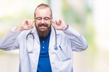 Yüksek sesle müzik gürültü rahatsız ifade parmaklarıyla kulaklarıyla kapsayan izole arka plan üzerinde tıbbi beyaz önlük giyen genç beyaz doktor adam. Sağır kavramı.