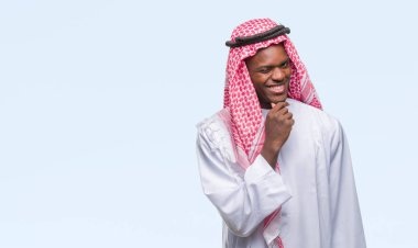 Geleneksel keffiyeh emin çapraz kollar ve çeneme kaldırdı el ile gülümseme ile kameraya bakarak izole arka plan üzerinde giyen genç Arapça Afrika adam. Pozitif düşünce.