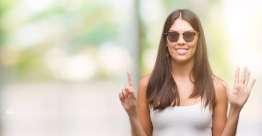 6 kendinden emin ve mutlu gülümseyerek sırasında gösterilen ve parmakları ile işaret genç güzel İspanyol giyen güneş gözlüğü numara.