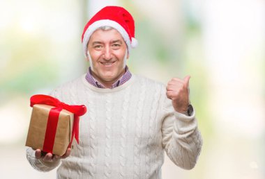 Üst düzey yakışıklı Noel şapka ve holding hediye işaret ve başparmak kadar mutlu yüz gülümseyen tarafı ile gösteren izole arka plan üzerinde giyen