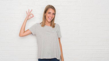 Üzerinde beyaz tuğla duvar gülümseyen güzel genç kadın el ve parmaklar ok işaretiyle yapıyor olumlu. Başarılı ifade.