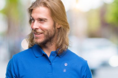 Yakışıklı delikanlı uzak tarafına yüzünde, doğal ifade gülümseme ile seyir izole arka plan üzerinde uzun saçlı. Kendine güvenen gülüyor.