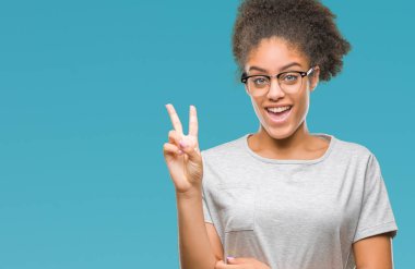Mutlu yüz zafer işareti yaparken kameraya göz kırpıyor ile gülümseyen izole arka plan üzerinde gözlük takan genç afro Amerikalı kadın. İki numaralı.