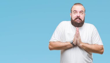 Yalvarıyor ve umut ifade yüzünde çok duygusal ve endişe ile birlikte elleriyle dua izole arka plan üzerinde rahat t-shirt giyen genç beyaz hipster adam. Bağışlanmak. Din kavramı.