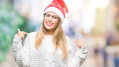 Yüzünde gülümseme ile kendinden emin görünüyorsun, kendini gururlu ve mutlu parmakları ile işaret izole arka plan üzerinde Noel şapka giyen genç güzel kadın.