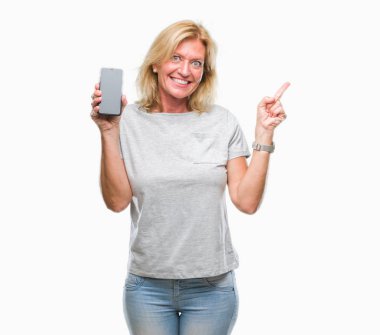 Orta yaş sarışın kadın gösteren boş ekran smartphone üzerinde izole arka tarafına el ve parmak ile işaret çok mutlu