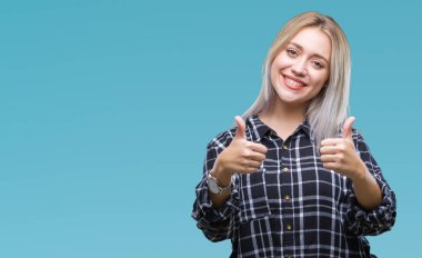 İzole edilmiş bir geçmişi olan genç sarışın kadın elleriyle olumlu bir jest yapmayı onaylıyor. Gülümsüyor ve başarı için seviniyor. Kameraya bak, kazanan jest..