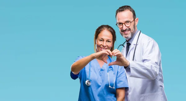 中年西班牙医生的伴侣夫妇穿着医疗制服在孤立的背景微笑着在爱显示心脏的象征和形状与手 浪漫的概念 — 图库照片