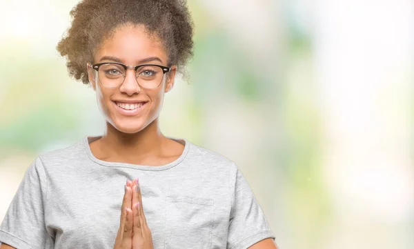 Young afro american woman wearing glasses over isolated background praying with hands together asking for forgiveness smiling confident.