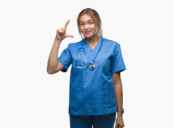 分離背景笑顔と自信を持ってサイズ記号を見ながら指とカメラをやって手でジェスチャーを外科医の制服を着て若い白人の医者の女性 測定概念 — ストック写真