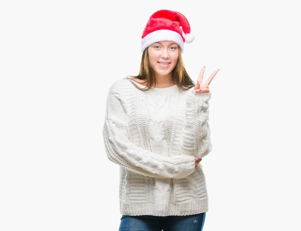 若い美しい白人女性の勝利のサインを行うカメラでウィンクしている幸せそうな顔を浮かべて隔離された背景にクリスマス帽子をかぶっています — ストック写真