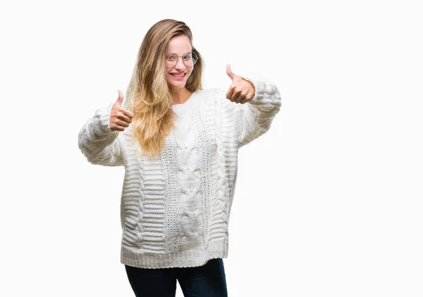 年轻美丽的金发女子穿着冬季毛衣和太阳镜在孤立的背景批准做积极的手势与手 竖起大拇指微笑和快乐的成功 看着相机 赢家手势 — 图库照片
