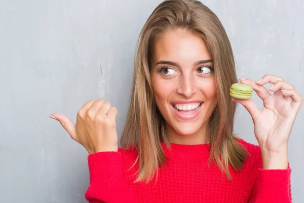 Mulher Bonita Sobre Parede Cinza Grunge Comer Macaron Verde Apontando — Fotografia de Stock