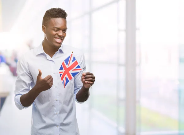 笑顔の サイン 優秀な兆候を親指をやって幸せなイギリスの旗を保持している若いアフリカ系アメリカ人 — ストック写真