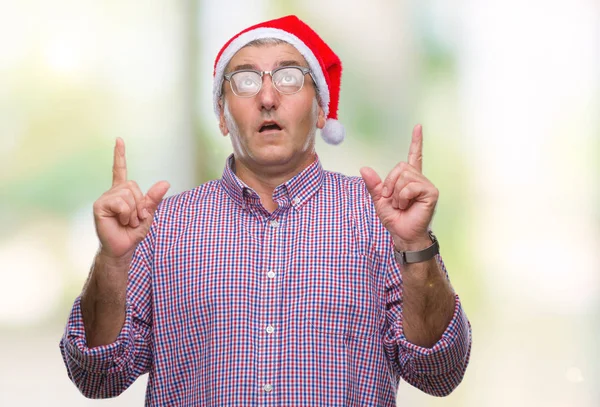 孤立した背景にクリスマスの帽子を着てハンサムな年配の男性びっくりし 驚き見て 指で指して 腕を上げた — ストック写真