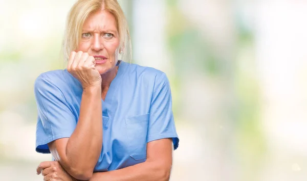中年の金髪女性が爪を噛んで口の中に不安や緊張で手を探している孤立した背景に医師看護師の制服を着てします 不安の問題 — ストック写真