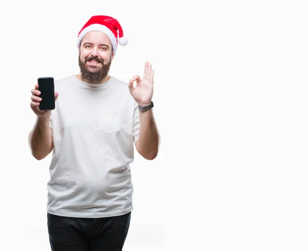 Junge Kaukasische Mann Mit Weihnachtsmütze Zeigt Smartphone Bildschirm Über Isoliertem — Stockfoto