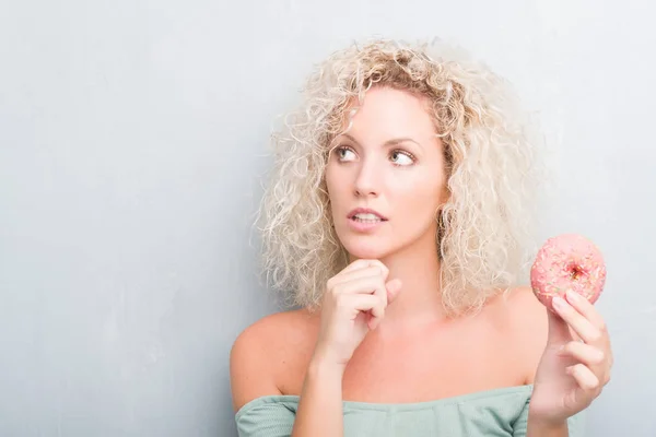 Joven Mujer Rubia Sobre Grunge Gris Fondo Comiendo Rosado Donut —  Fotos de Stock