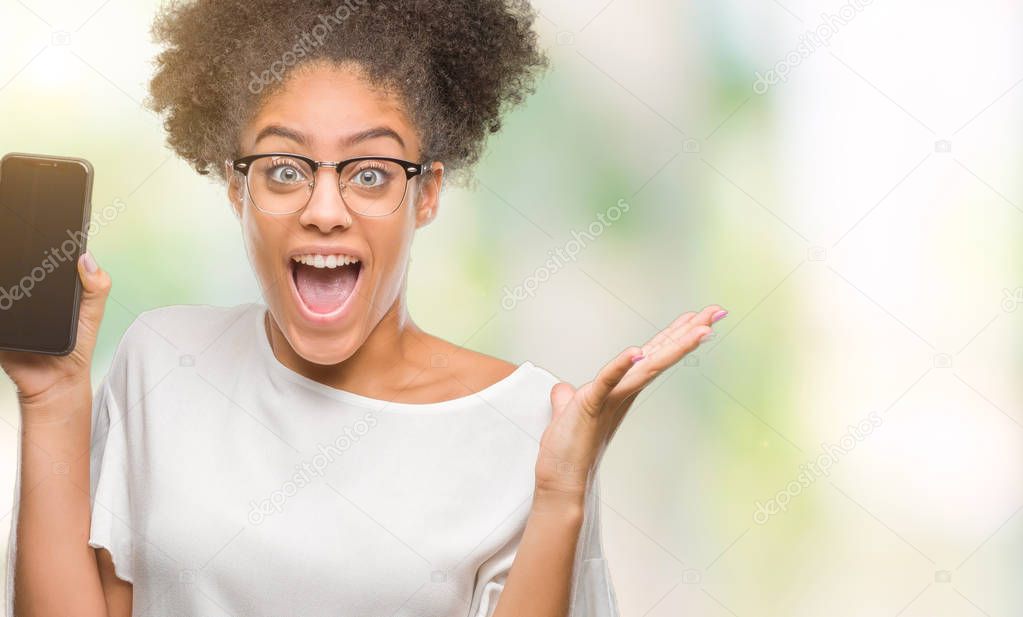 Young beautiful afro american showing smartphone screen over isolated background very happy and excited, winner expression celebrating victory screaming with big smile and raised hands