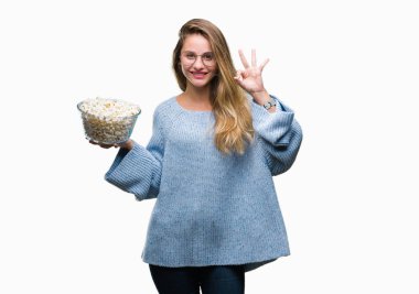 Genç güzel sarışın kadın parmakları, mükemmel sembolü olan ok işareti yapıyor izole arka plan üzerinde patlamış mısır yemek