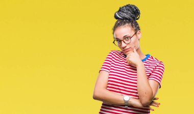Genç saç Afro-Amerikan Kız çene düşünme hakkında soru, dalgın ifade üzerine el ile izole arka plan üzerinde gözlük takan örgülü. Düşünceli yüzüyle gülümsüyor. Şüphe kavramı.