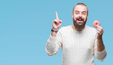 Genç beyaz hipster man yemek tatlı çörek üzerinde arka plan ile bir fikir ya da gülen yüz, bir numara ile parmak işaret soru sürpriz izole