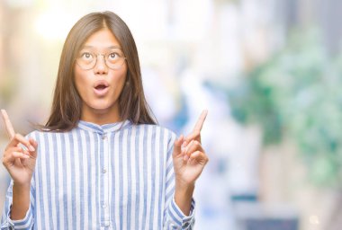 Genç Asyalı kadın izole arka plan üzerinden hayran ve yukarıya bakıp parmakları ile işaret şaşırttı ve silah kaldırdı.