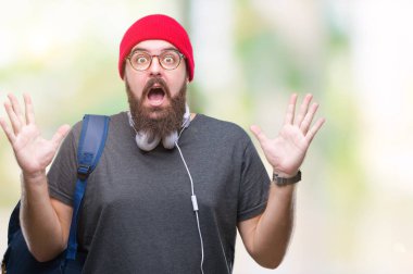 Üzerinde kırmızı yün kap ve sırt çantası giyen genç hipster adam deli kutluyor arka plan izole ve başarı için kaldırdı kollarını açarak hayrete ve heyecanlı çığlık gözleri açık. Kazanan kavramı