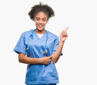 Kameraya bakarak yan el ve parmak ile işaret eden genç afro Amerikalı doktor kadın yüzünde kocaman bir gülümseme ile izole arka plan üzerinde.