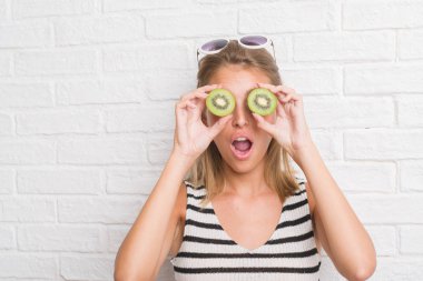 Beyaz tuğla duvar yeme üzerinde güzel genç kadın yeşil kivi bir sürpriz yüz, korkuyor ve heyecanlı korku ifadesi ile şok korkmuş