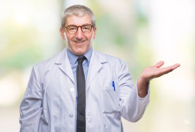 Yakışıklı kıdemli Doktor, neşeli sunulması ve kameraya bakarak avucunun ile işaret gülümseyen arka plan üzerinde beyaz önlük giyen bilim adamı profesyonel adam izole.