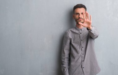 Genç yetişkin adam dur yapıyor gri grunge duvardan ayakta elin avuç ile şarkı. Negatif ve ciddi bir jest yüz ifadesiyle uyarı.