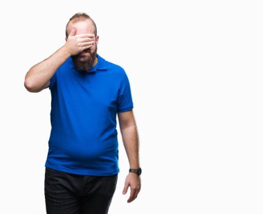 Genç beyaz hipster adam gülümsüyor ve gözleri için sürpriz kapsayan yüz el ile gülüyor izole arka plan üzerinde mavi tişört giyiyor. Kör kavramı.