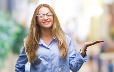 Neşeli sunulması ve kameraya bakarak avucunun ile işaret gülümseyen izole arka plan üzerinde gözlük takan genç güzel sarışın iş kadını.