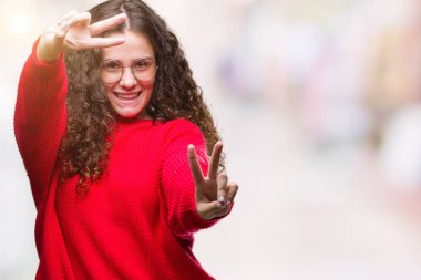 Güzel esmer kıvırcık saçlı Genç kız zafer işareti yapıyor parmak gösterilen kamera seyir gülümseyen izole arka plan üzerinde gözlük ve kış kazak giyiyor. İki numaralı.