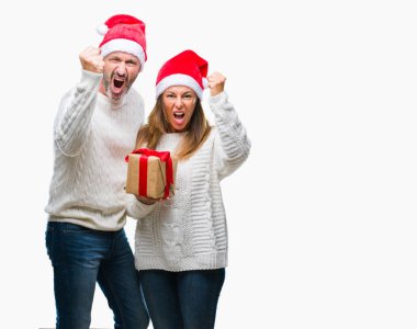 Orta yaş İspanyol çift giyen Noel şapka ve holding hediye izole arka rahatsız üzerinde ve öfke ile sinirli bağırarak, deli ve ile bağırmaya elini, öfke kavramı kaldırdı