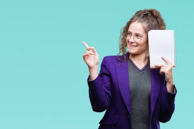Okul bir defter izole arka plan üzerinde çok mutlu el ve parmak ile tarafına işaret tutan üniforma giyen genç esmer öğrenci kız