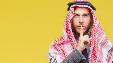 Genç yakışıklı Arap adam uzun saçlı dudaklarında parmak ile sessiz olmanı izole arka plan üzerinde keffiyeh giyiyor. Sessizlik ve gizli kavramı.