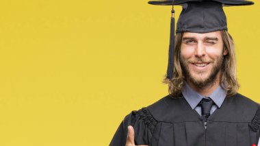 Genç yakışıklı adam uzun saçlı izole arka plan üzerinde derecesi büyük gülümseme ok işareti, başparmak ile parmak, mükemmel işareti yapıyor ile mutlu tutarak yüksek lisans