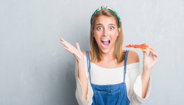 Grunge güzel genç kadın gri duvar büyük gülümseme ile çığlık ve ellerini kaldırdı kazanan ifade kutluyor zafer pepperoni pizza dilimi çok mutlu ve heyecanlı, yemek