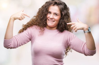 Yüzünde gülümseme ile kendinden emin görünüyorsun, kendini gururlu ve mutlu parmakları ile işaret izole arka plan üzerinde pembe kazak giyen güzel esmer kıvırcık saçlı Genç kız.