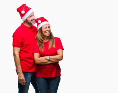 Orta yaş İspanyol çift uzakta yanında seyir izole arka plan üzerinde Noel şapka yüzünde, doğal ifade gülümse. Kendine güvenen gülüyor.