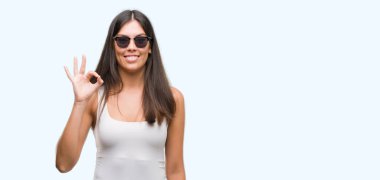 Genç güzel İspanyol el ve parmaklar ok işaretiyle yapıyor olumlu gülümseyen güneş gözlüğü takıyor. Başarılı ifade.