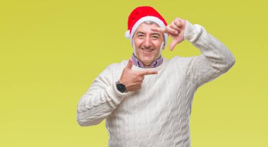 Elle yapma çerçeve ve parmakları ile mutlu yüz gülümseyen izole arka plan üzerinde Noel şapka giymiş yakışıklı komuta sizde. Yaratıcılık ve Fotoğrafçılık kavramı.