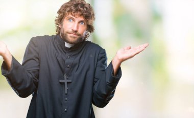 Yakışıklı İspanyol Katolik rahip adam izole arka plan clueless ve şaşkın bir ifadeyle kollar ve eller kaldırdı. Şüphe kavramı.