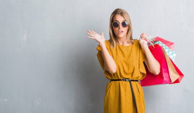 Güzel genç kadın alışveriş torbaları büyük gülümseme ile çığlık zaferini kutluyor ve ellerini kaldırdı satış çok mutlu ve heyecanlı, kazanan ifade üzerinde tutarak grunge gri duvarın üzerinden