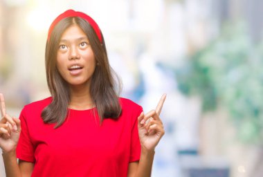 Genç Asyalı kadın izole arka plan üzerinden hayran ve yukarıya bakıp parmakları ile işaret şaşırttı ve silah kaldırdı.