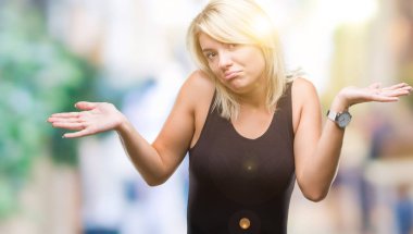 Zarif giyen genç güzel sarışın çekici kadın elbise üzerinde izole arka plan clueless ve şaşkın bir ifadeyle kollar ve eller kaldırdı. Şüphe kavramı.