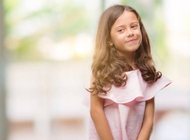 Esmer Latin kız uzak tarafına yüzünde, doğal ifade gülümseme ile seyir pembe elbise. Kendine güvenen gülüyor.